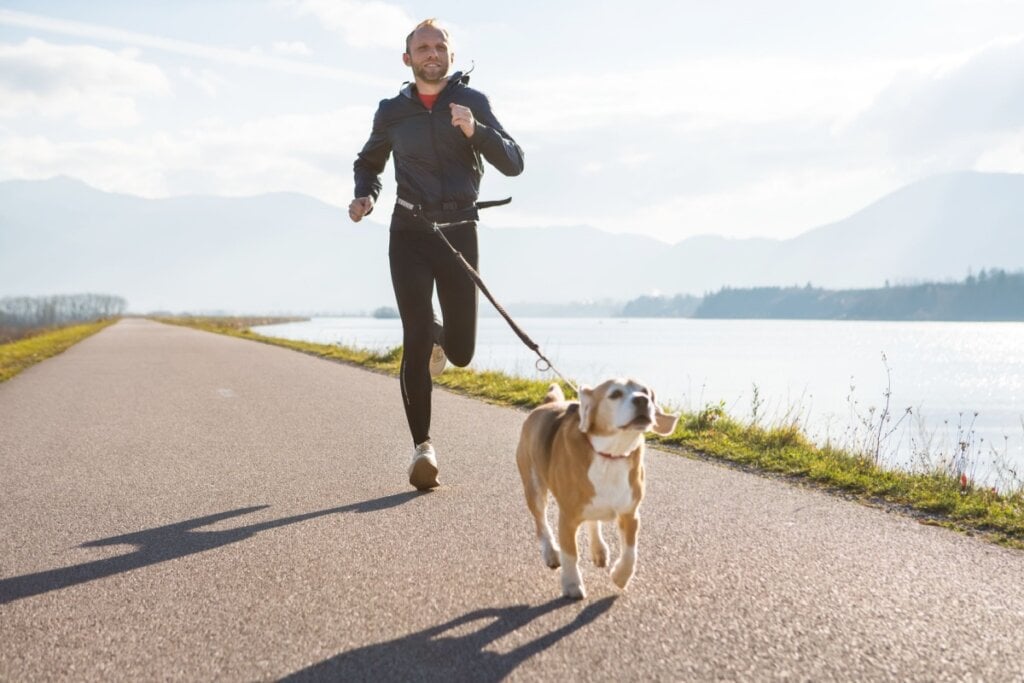 Homem vestindo legging e blusa de frio praticando canicross com um cachorro em frente a um lago