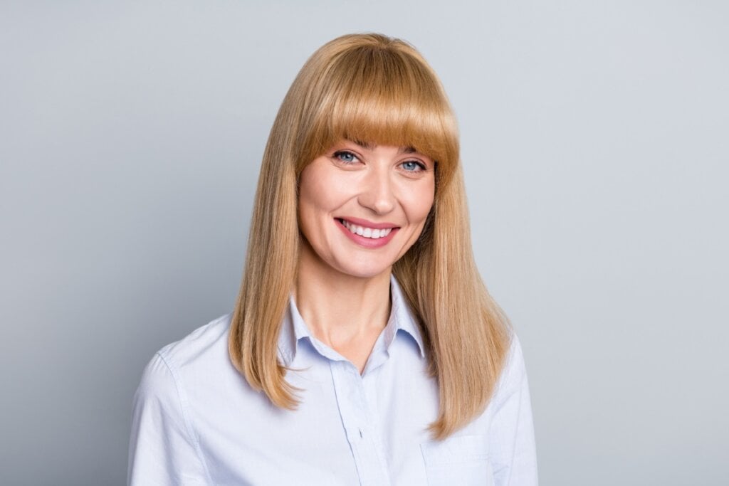 Mulher com cabelo loiro médio com franja côncava sorrindo