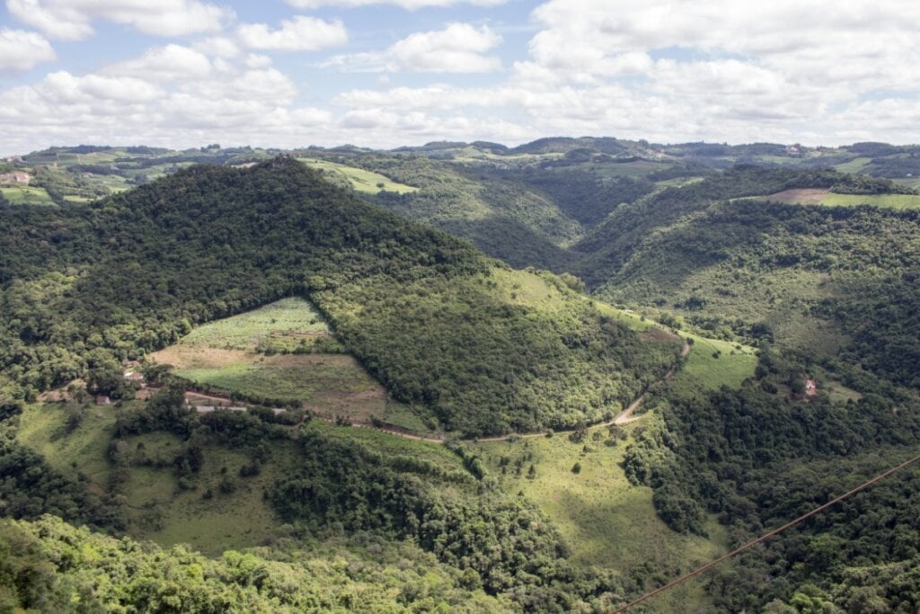 Vista da Serra Gaúcha com montanhas com árvores e um céu com nuvens brancas