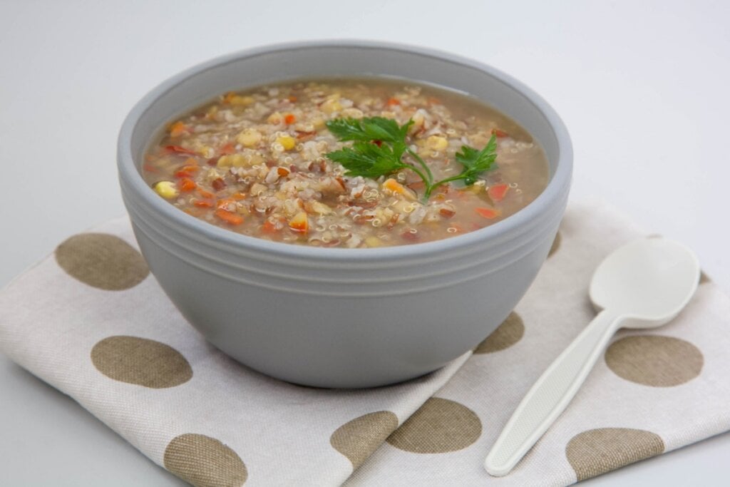 Recipiente cinza com sopa de lentilha com cenoura, milho-verde, arroz vermelho, lentilha e salsinha