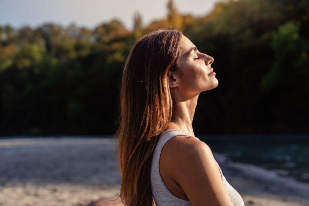 Mulher virada de lado, e com os olhos fechados, tomando sol ao ar livre