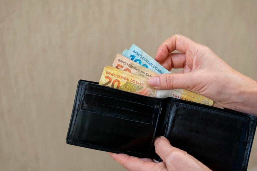 Mão segurando uma carteira preta com notas de dinheiro saindo dela 
