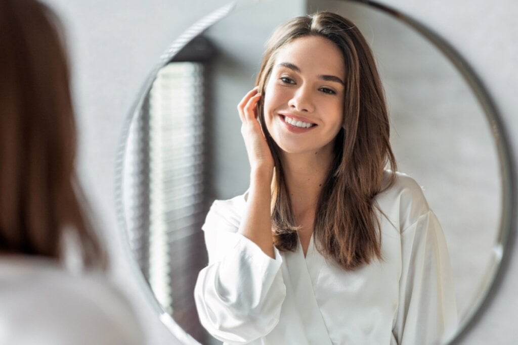 Mulher sorrindo e olhando o rosto em um espelho