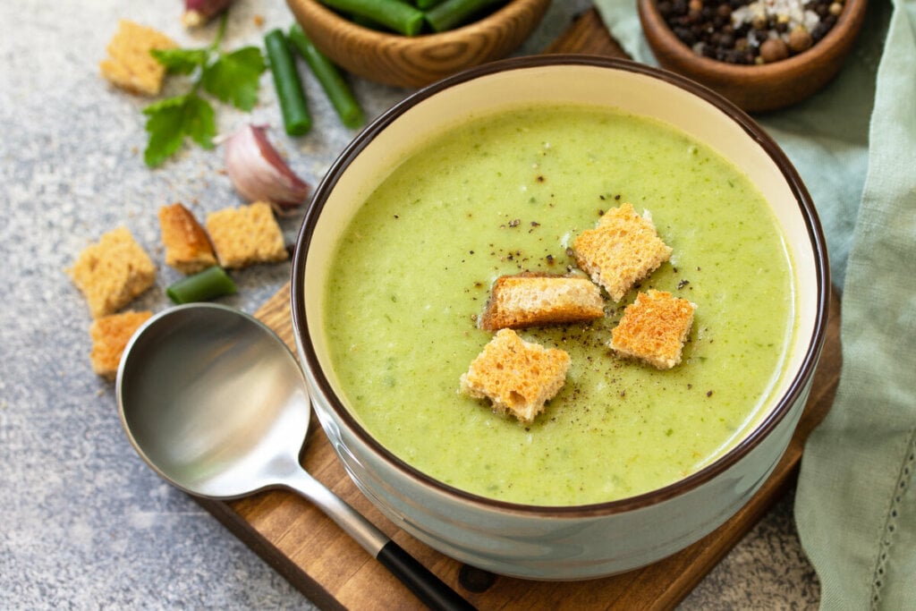 Panela branca com sopa de espinafre em cima de uma tÃ¡bua de madeira
