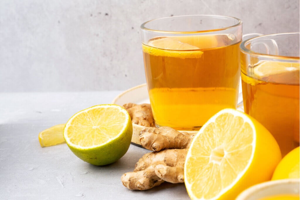 Copo transparente com ch&Atilde;&iexcl; de gengibre e lim&Atilde;&pound;o em cima de uma mesa com rodelas de lim&Atilde;&pound;o e gengibre