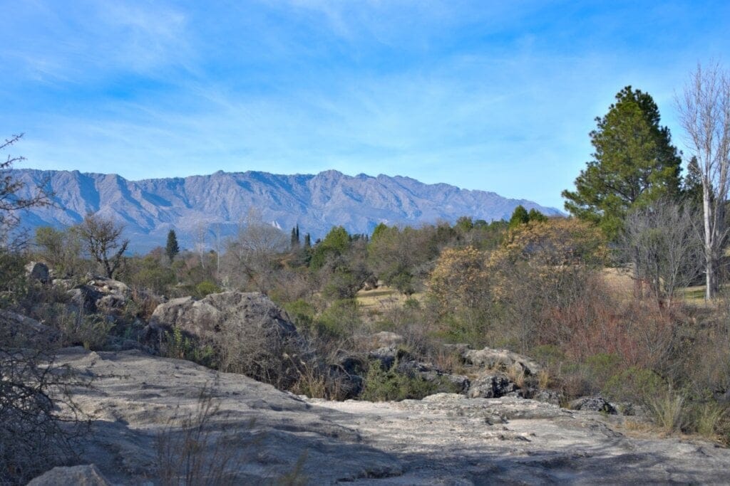 Paisagem com a cadeia de montanhas conhecida como Sierras de Córdoba, árvores e solo rochoso à s margens do rio Cruz del Eje, na provÃncia de Córdoba, Argentina.