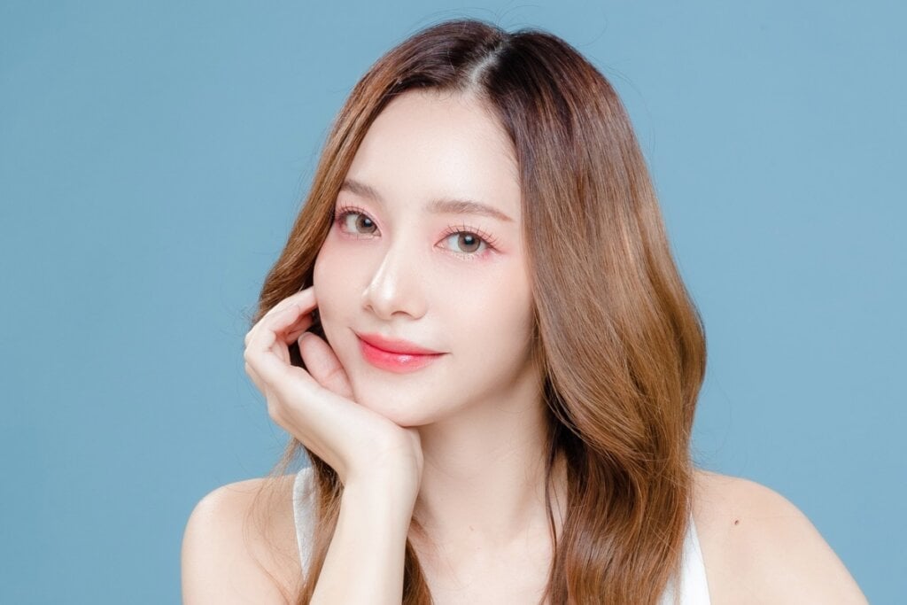 Mulher de cabelo castanho longo sorrindo, usando maquiagem leve e com a mÃ£o no queixo