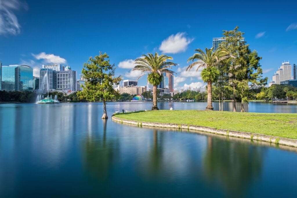 Vista de lago em parque na cidade de Orlando com diversos coqueiros e uma parte de grama ao lado do lago