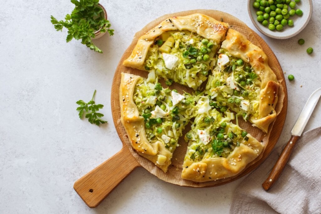Torta aberta de repolho, ervilha e queijo feta fatiada em tÃ¡bua redonda