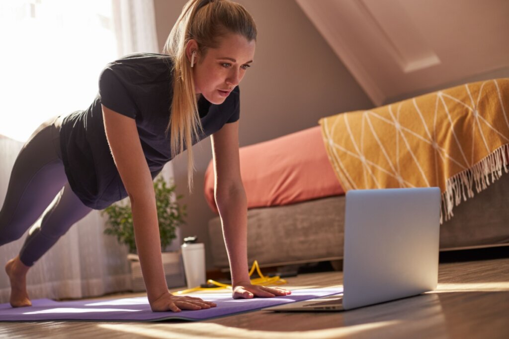 Mulher fazendo exercÃcio em casa e em frente a um notebook
