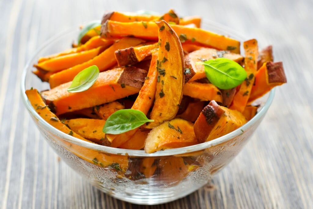 recipiente de vidro com palitos de batata-doce laranja assada com ervas e folhas de manjericÃ£o