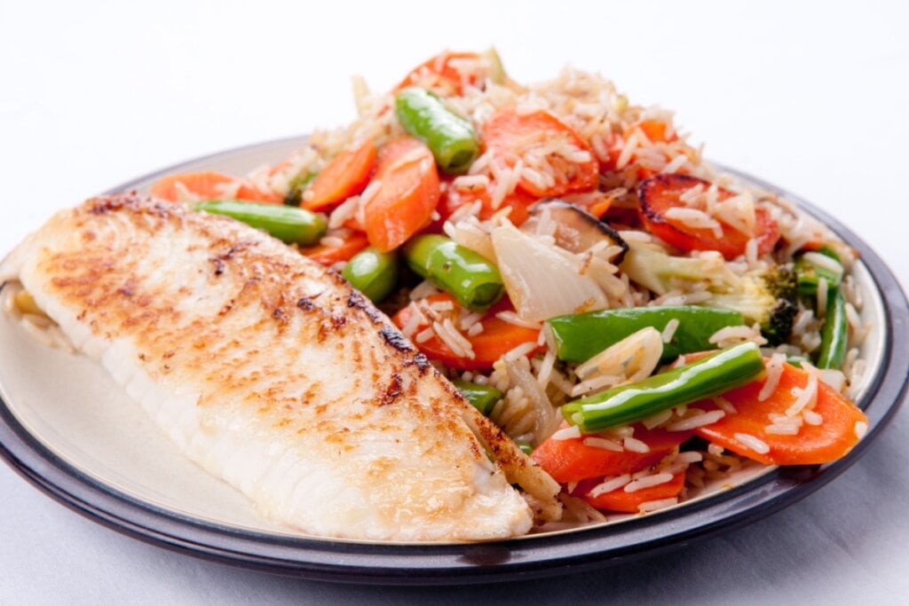 Prato branco com filÃ© de tilÃ¡pia e arroz com legumes