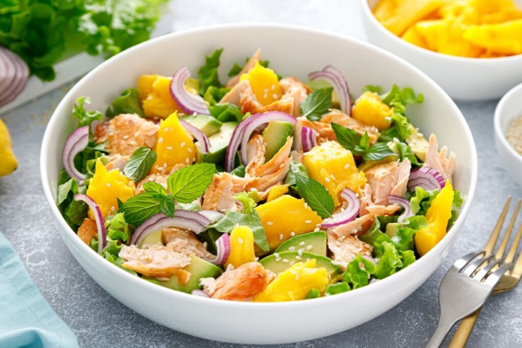 Salada de salm&Atilde;&pound;o com manga e abacate servido em tigela funda de cer&Atilde;&cent;mica em cima de mesa de pedra