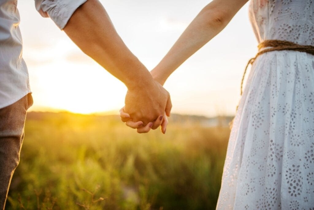 Foto com foco nas mãos dadas de um casal ao pôr do sol 