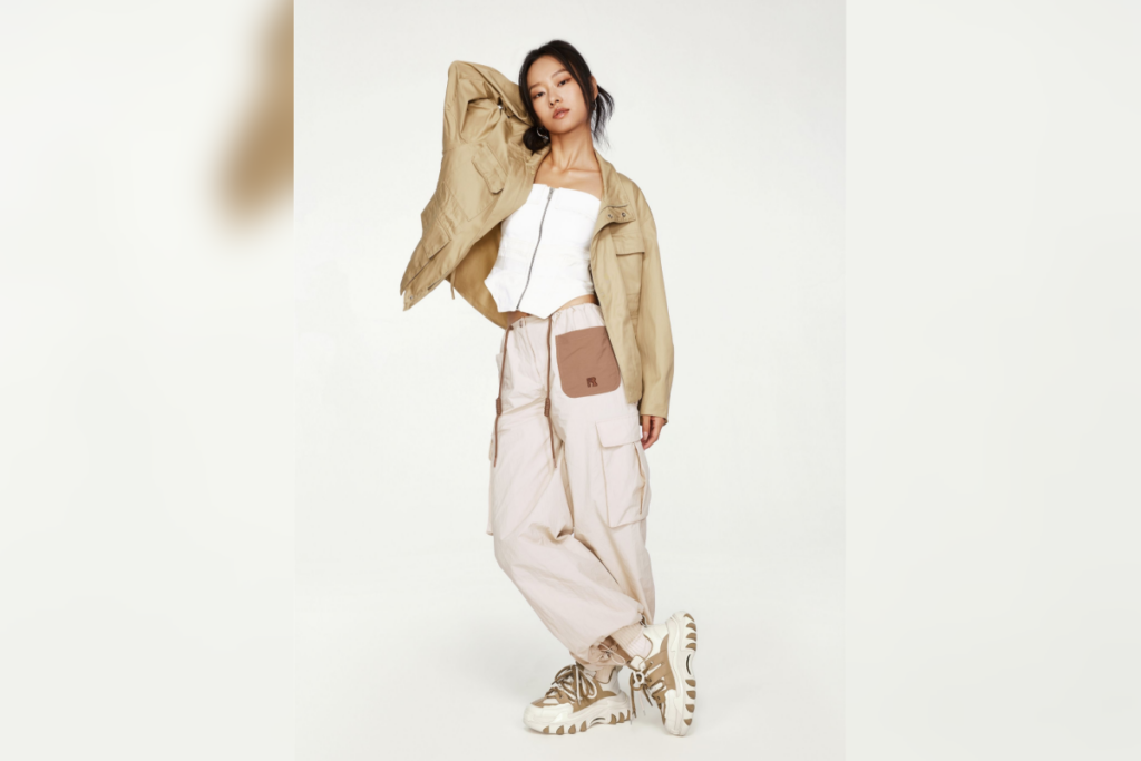 Mulher posando com jaqueta clara, calça cargo larga e tênis chunky em estúdio de fundo branco