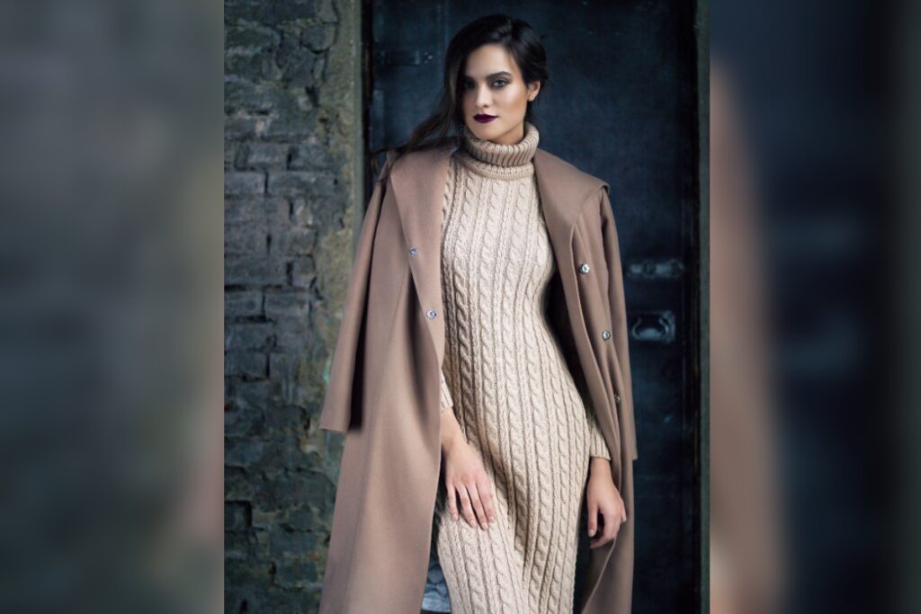 Mulher de vestido longo de tricô e casaco sobre os ombros em ambiente com tijolos