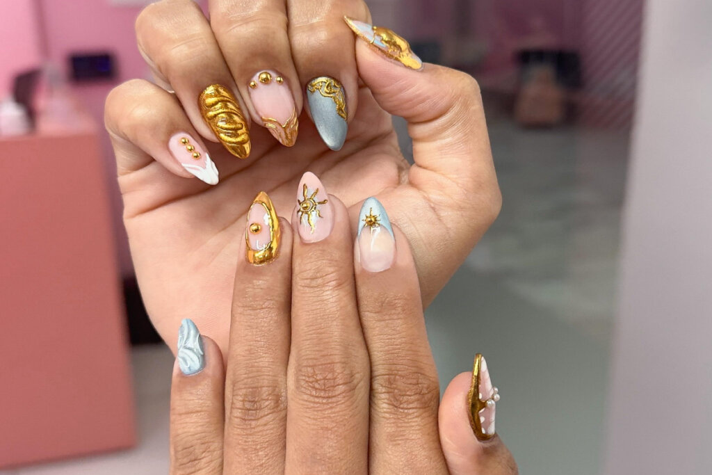 duas mÃ£os com unhas em tons de amarelo, azul e rosa com aplicaÃ§Ãµes 3D
