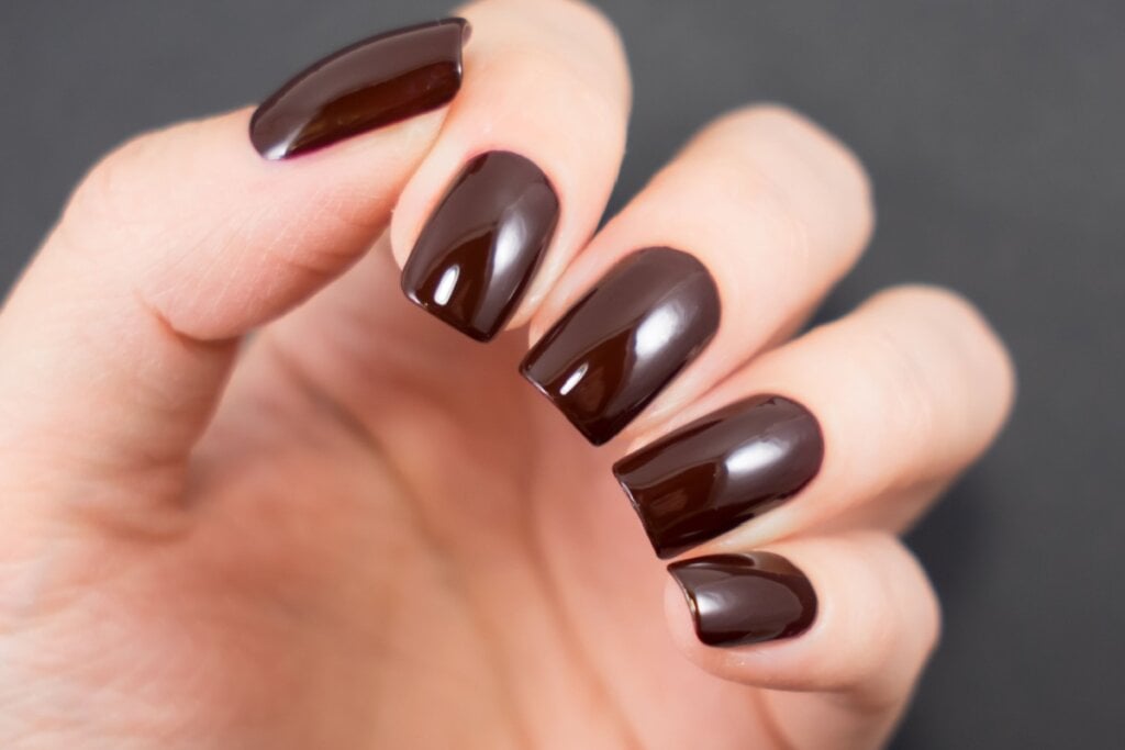 mÃ£o com unhas femininas em tom de marrom-escuro