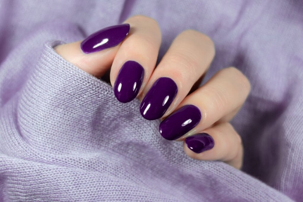mÃ£o feminina com tecido roxo e unhas com esmalte roxo