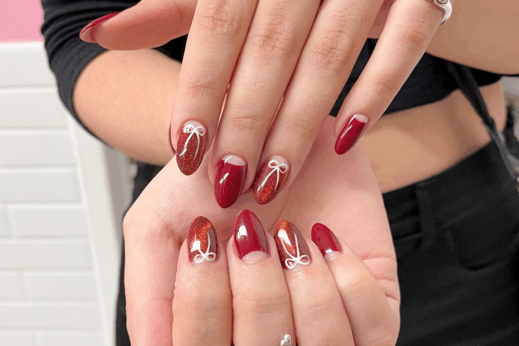 duas mÃ£os com unhas em tons de vermelho e marrom e desenhos de laÃ§os