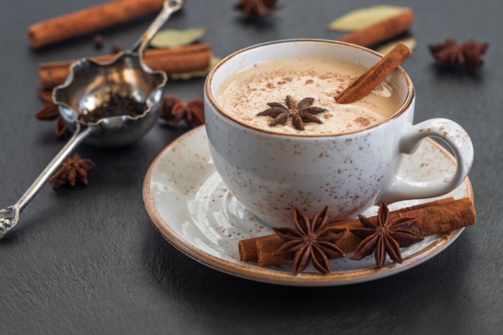Chai latte servido em xÃ­cara estampada de cerÃ¢mica em cima de mesa de madeira preta com castanha e cravos-da-Ã­ndia.