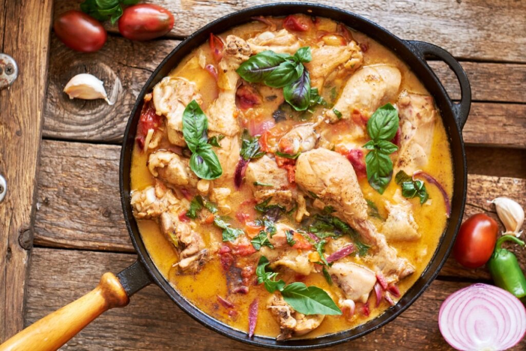 imagem de panela preta com pedaÃ§os de galinha com molho laranja com tomate e manjericÃ£o