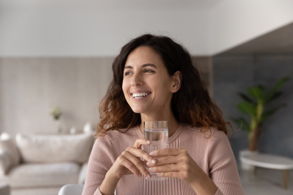 Mulher sorrindo, sentada e segurando um copo de vidro com Ã¡gua