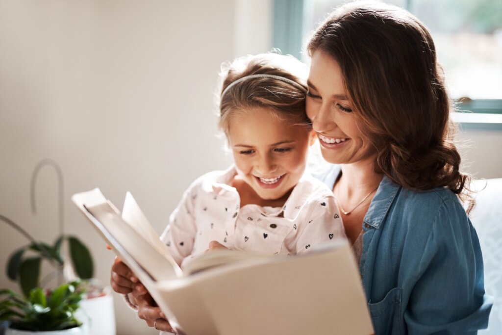 MÃ£e lendo livro com filha; ambas sorridentes