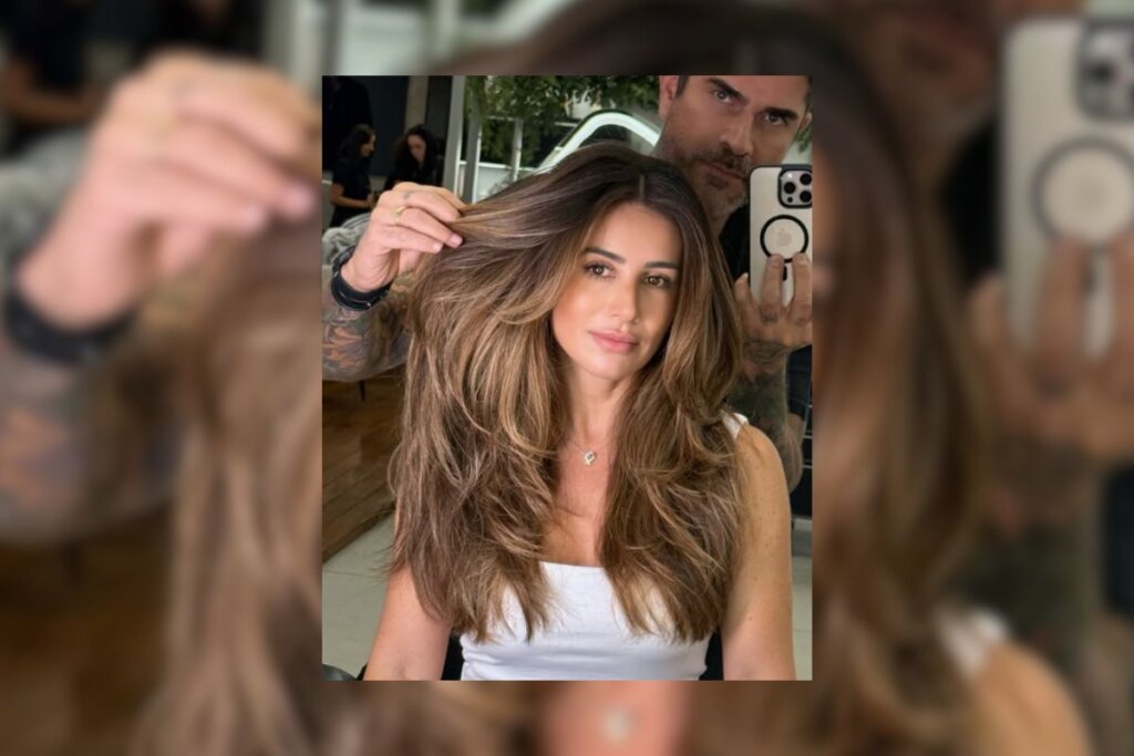 Mulher com cabelo longo com mechas em chocolate e um homem do lado segurando uma mecha do seu cabelo