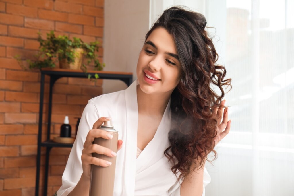 mulher de roupÃ£o branco aplicando spray no cabelo cacheado e sorrindo