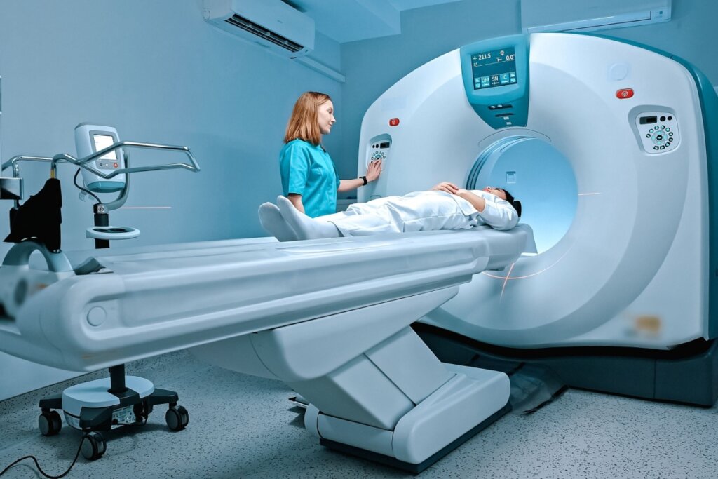 Pessoa deitada fazendo ressonância magnética e uma médica em pé do lado