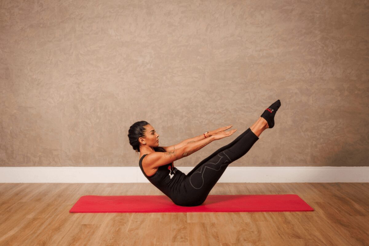 Mulher fazendo exercÃcios de pilates no chão em tapete vermelho usando roupas de academia preta