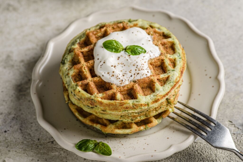 Waffle de abobrinha servido com molho de iogurte em prato de cer&Atilde;&cent;mica branco em cima de mesa de pedra