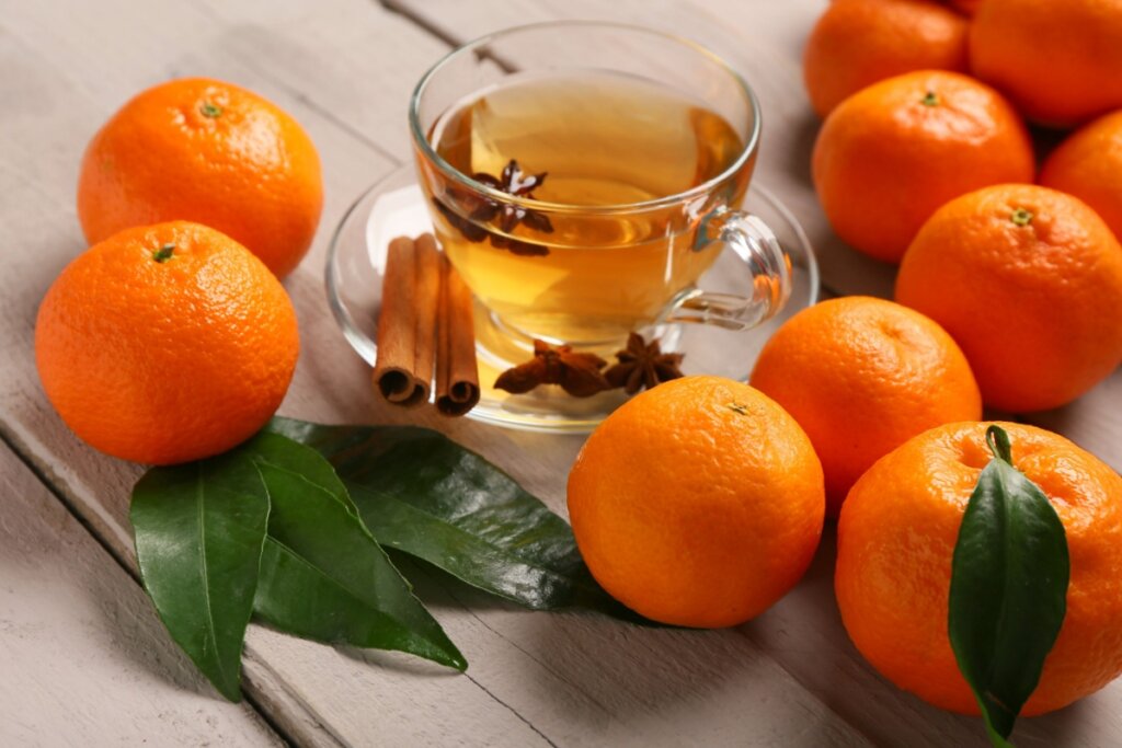 XÃcara de vidro com chá de tangerina com anis-estrelado e canela em cima de uma mesa de madeira com tangerinas