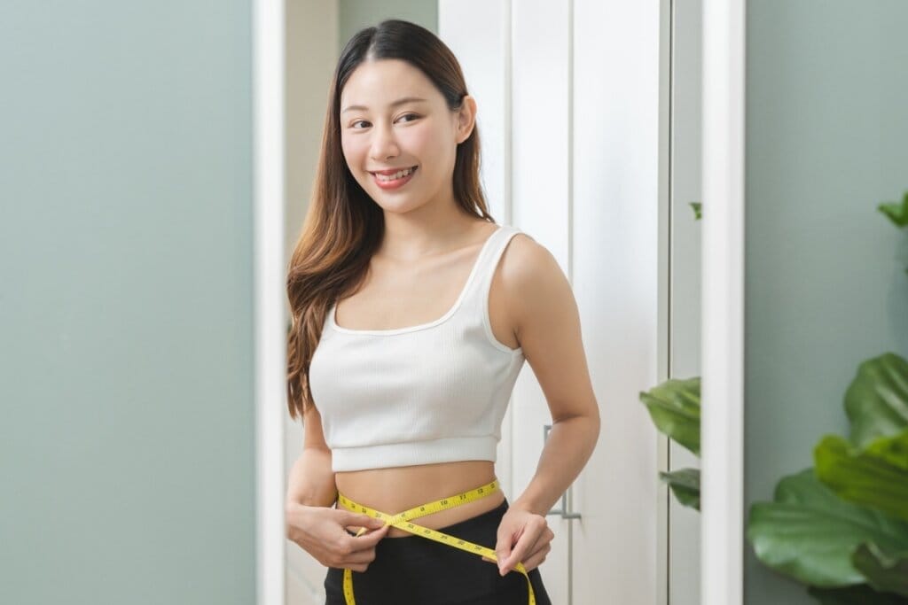 Mulher medindo a cintura com uma fita mÃ©trica amarelo em frente a um espelho