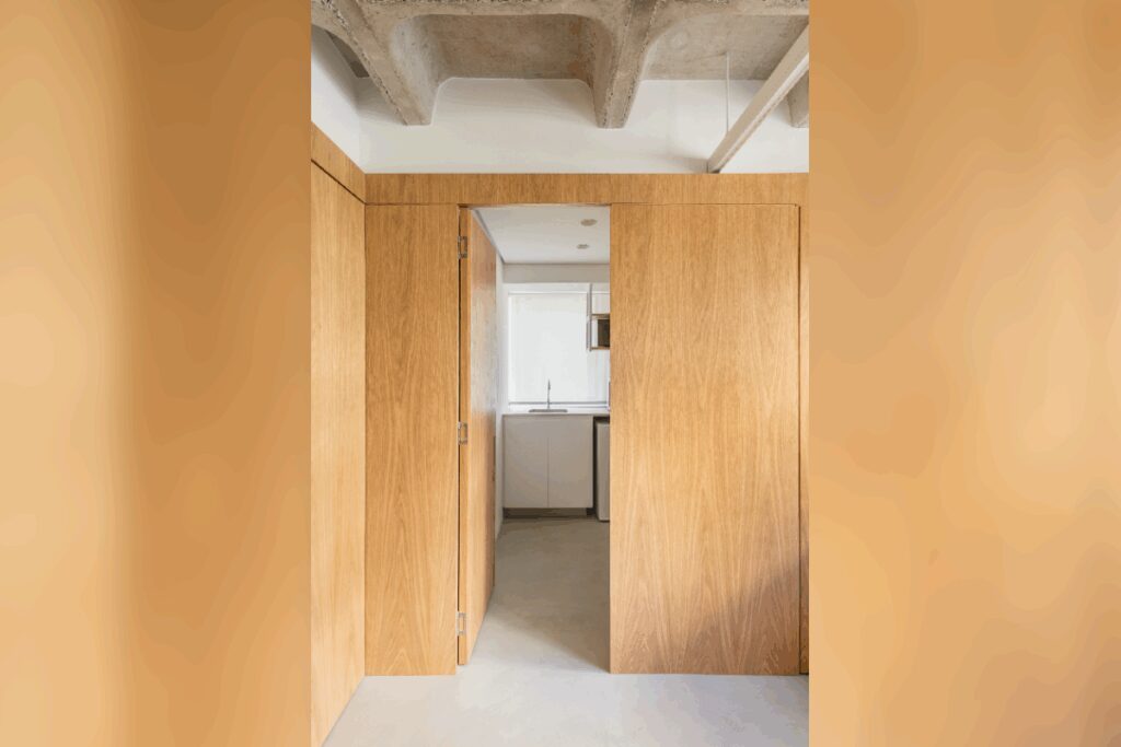 Porta camuflada em painel de madeira clara conduzindo a outro ambiente em apartamento contemporÃ¢neo