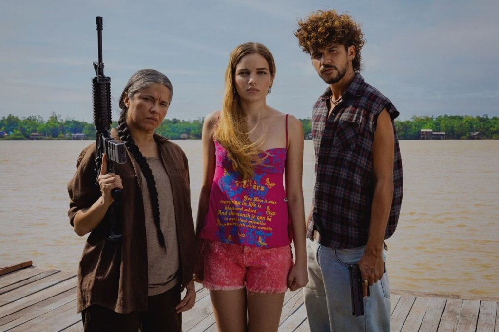 Três personagens da série "Pssica" em pé em frente a um rio na Amazônia