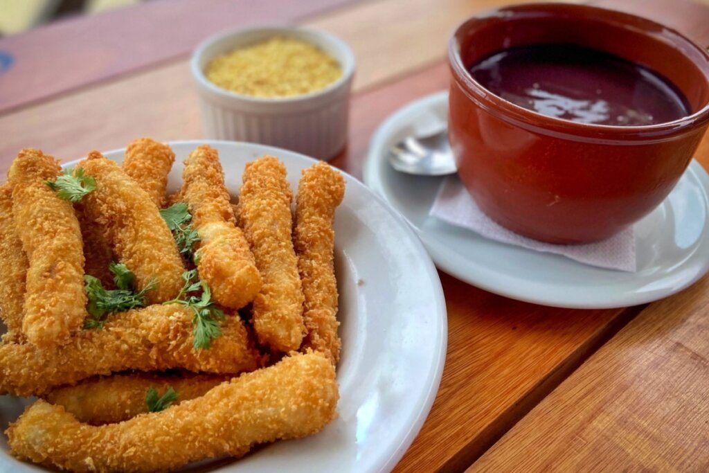 Prato com peixe empanado e recipiente marrom com creme de açaà em cima de uma mesa de madeira