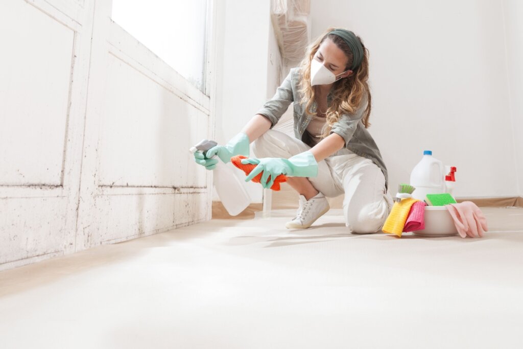 Mulher usando luvas, mÃ¡scara e produtos de limpeza enquanto remove mofo