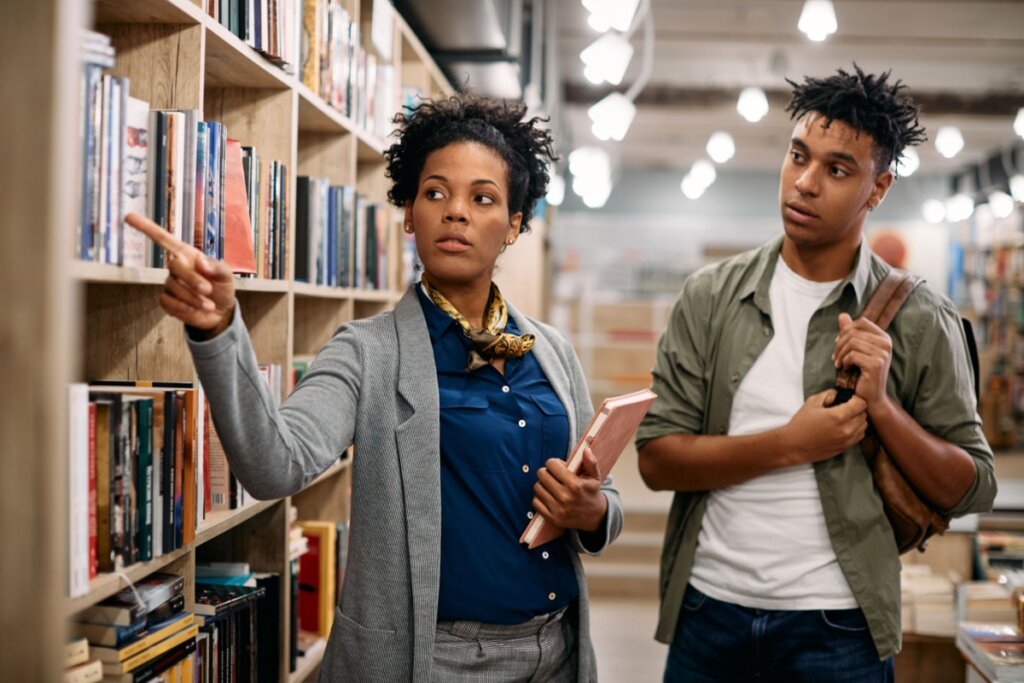bibliotecÃ¡ria mostrando livros na prateleira para homem