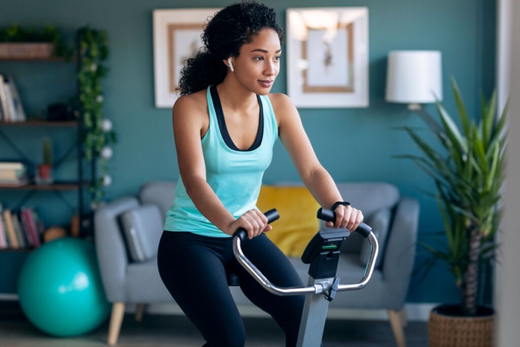 Jovem com o cabelo cacheado, usando roupas de academia fazendo exercÃcio em bicicleta ergométrica