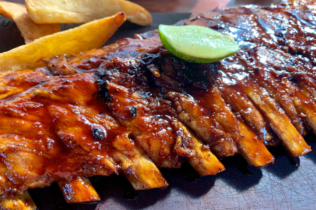 Costela com molho barbecue em cima de uma superfÃcie preta e com a fatia de um limão em cima