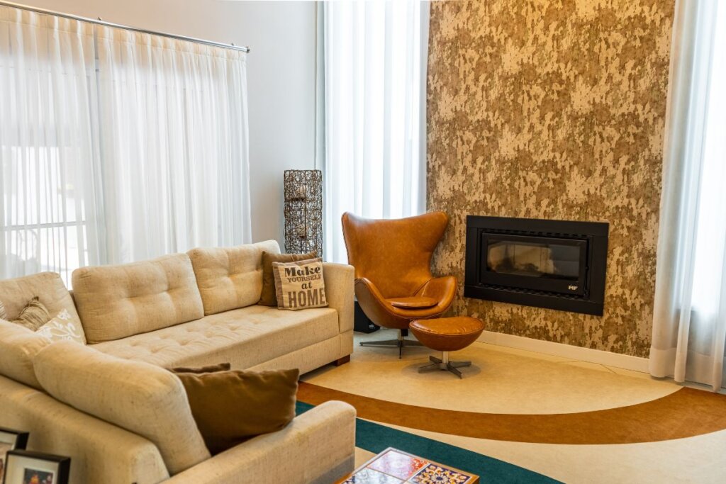 Sala de estar com janela com cortina branca, sofÃ¡ na mesma cor e lareira