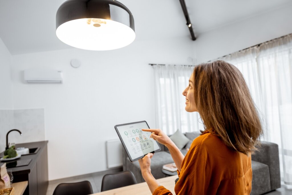 Mulher com o cabelo claro, liso, curto e solto com um tablet na mão automatizando luz da sala