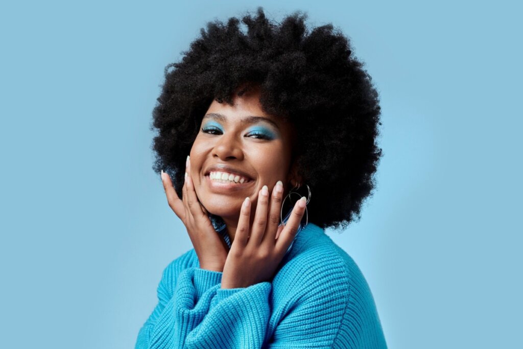 Jovem com o cabelo cacheado curto, usando sombra azul e blusa azul