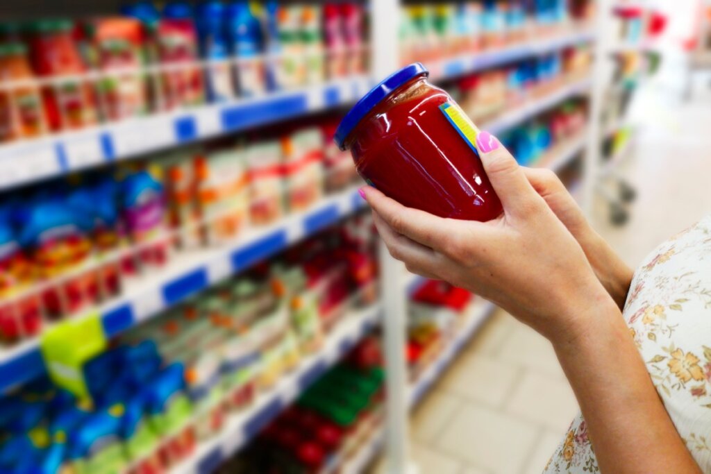 Mão segurando um recipiente com molho em um supermercado