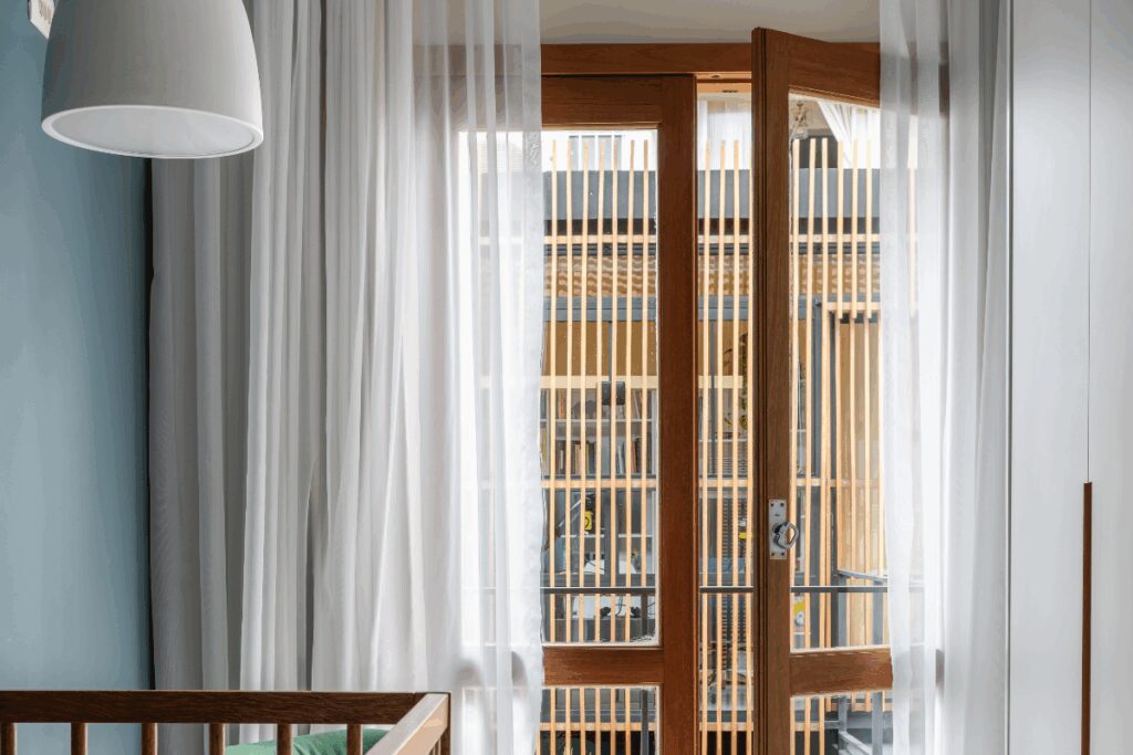 Porta de madeira com vidro em sacada de quarto com cortina branca