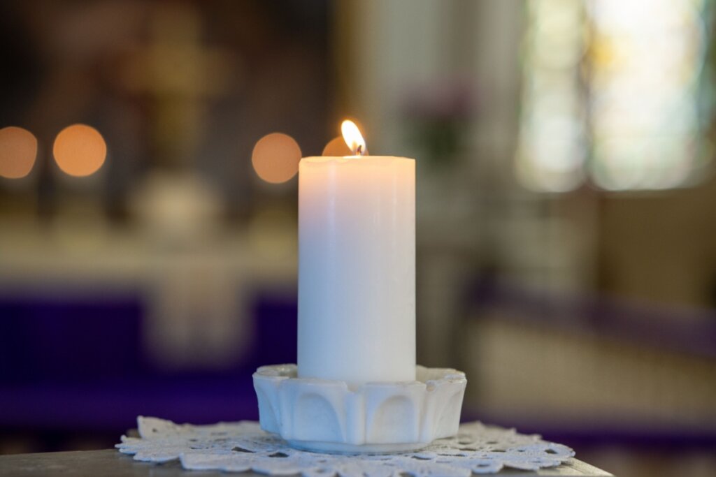 Imagem de uma vela branca acesa em cima de um recipiente de vidro