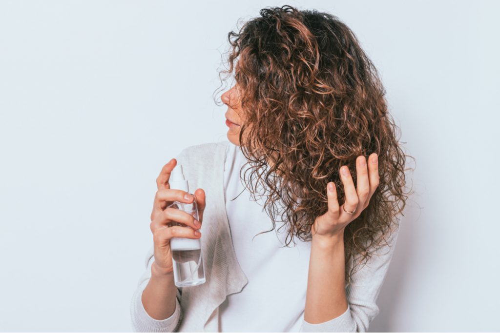 Mulher fazendo finalizaÃ§Ã£o no cabelo ondulado com um spray