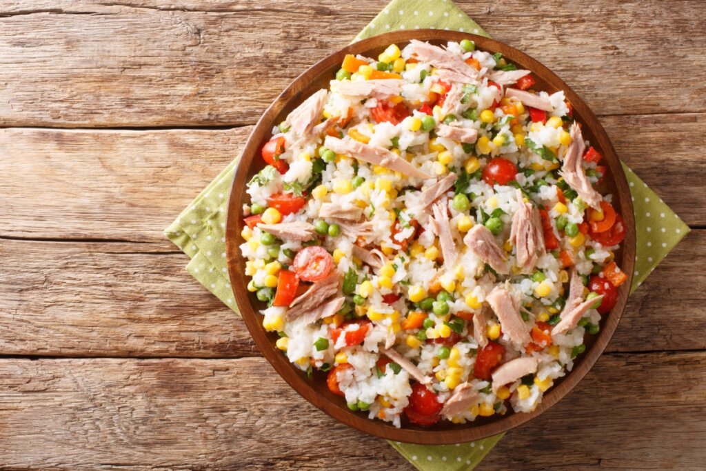 Salada de arroz com atum e legumes em recipiente marrom em cima de pano verde com cÃrculos brancos sob superfÃcie de madeira